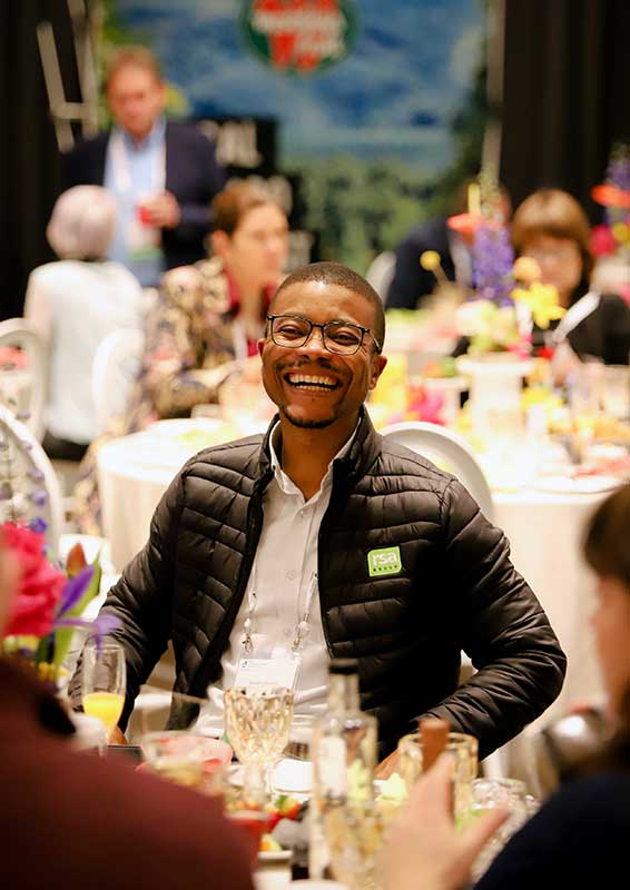 A gentleman with a large smile sitting at table in a banquet room.